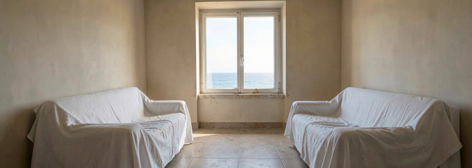 An empty apartment with furniture under white dust sheets and a key on the windowsill overlooking the sea