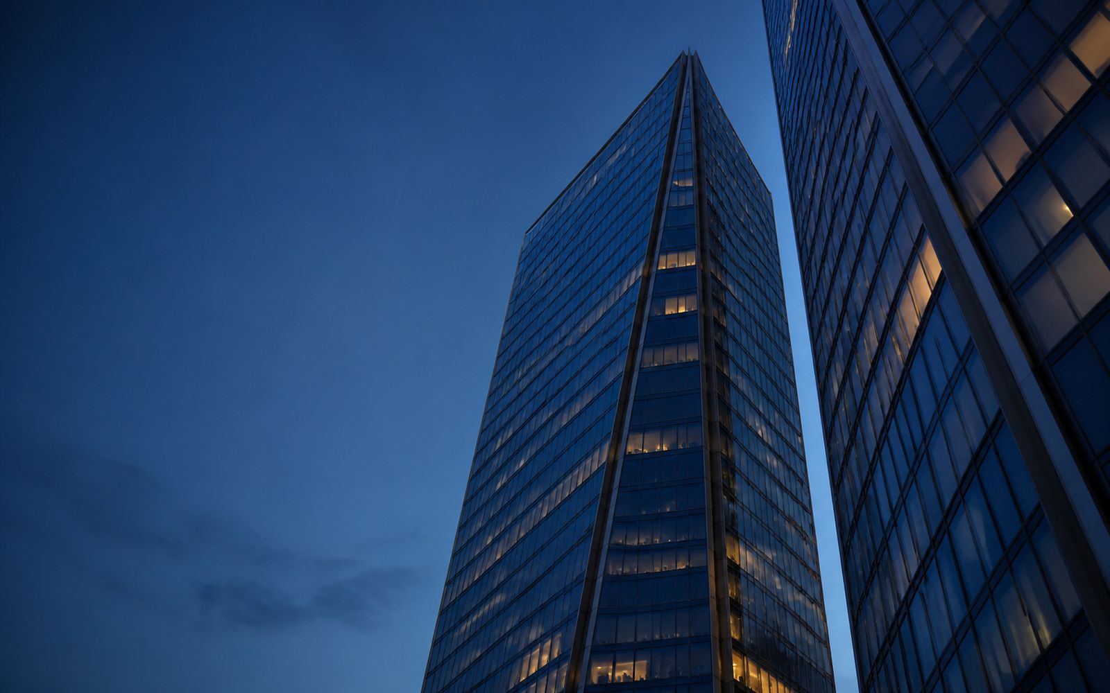 Two glass office towers seen from below, meeting at a narrow sky gap