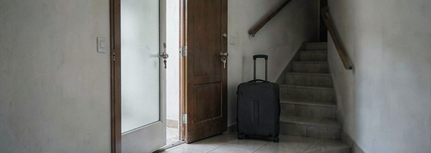 An open apartment door with a key left in the lock and a packed suitcase on the landing